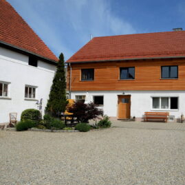 Seitenansicht eines Bauernhauses. Auf dem alten Stallgebäude wurde ein weiteres Stockwerk gesetzt. Neue Holzfassade harmoniert mit altem weiß verputzten Gebäude