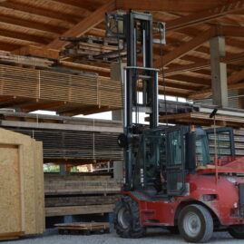 Seitenansicht eines Staplers der gerade Holzpalääten in Lagerhalle lädt