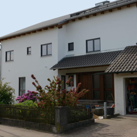 Aufgestockter Bungalow, Übergang nicht sichtbar. Weiß verputztes Gebäude in Seitenansicht